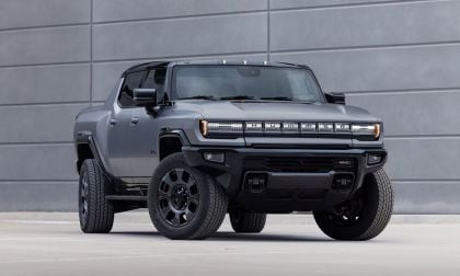 A sleek, grey Hummer EV pickup truck parked in front of a modern, minimalist grey wall, showcasing its bold design and large tires.
